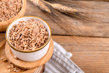 Wholegrain uncooked raw spelt farro in bowl on the wooden background, food cereal background, close up