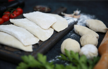 The national dish is Tatar cuisine. Preparation. The culinary process of chebureks. Raw dough with minced meat, rolling pin, flour, herbs, tomatoes, spices and garlic. Background image, copy space