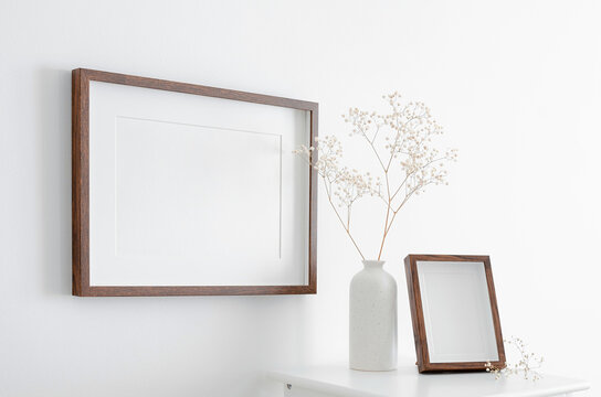 Blank landscape and portrait frames mockup on white wall with dry gypsophila plant decorations. Minimalistics scandinavian style interior with artwork mockup.