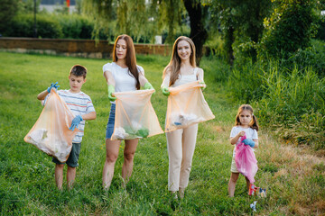 Naklejka premium A group of girls with children at sunset are engaged in garbage collection in the park. Environmental care, recycling.