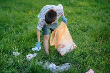 A seven-year-old boy at sunset is engaged in garbage collection in the park. Environmental care,...
