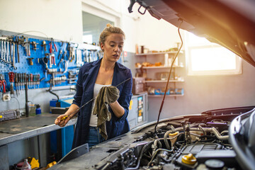Mechanic working under the hood at the repair garage. Portrait of a happy mechanic woman working on...