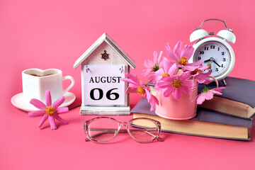 Calendar for August 6 : the name of the month of August in English, the numbers 0 6, a cup of tea, books, a bouquet of pink flowers, glasses for vision, an alarm clock on a pink background