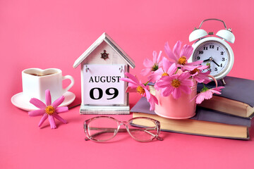 Calendar for August 9 : the name of the month of August in English, the numbers 0 9, a cup of tea, books, a bouquet of pink flowers, glasses for vision, an alarm clock on a pink background