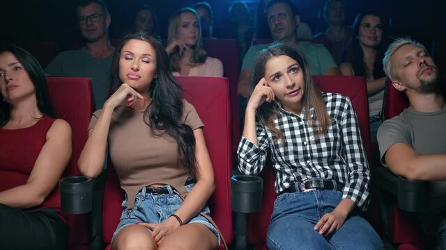 Two upset woman friends watching bad film with unpleasant negative emotion bored at cinema