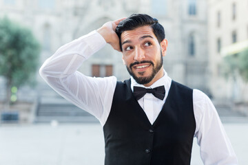 Handsome young man in formalwear adjusting his hairstyle and smiling standing outdoors