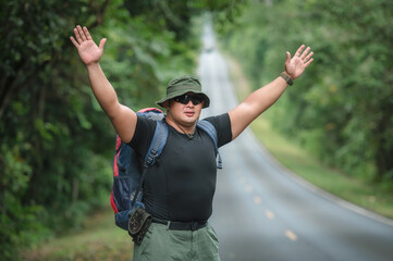 Fototapeta premium Backpackers travel by hiking and hitchhiking tourists. to travel to the destination. Tourists hitchhike, waved to help me, sat exhausted on the roadside to travel on foot in Khao Yai National Park.