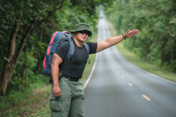Fototapeta premium Backpackers travel by hiking and hitchhiking tourists. to travel to the destination. Tourists hitchhike, waved to help me, sat exhausted on the roadside to travel on foot in Khao Yai National Park.