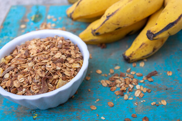 GRANOLA EM TIGELA BRANCA COM BANANAS NO FUNDO.