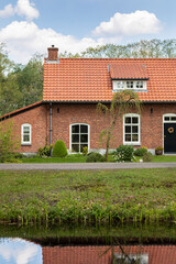 Dutch authentic house near the river with reflections in the water, surrounded by trees and greenery on a sunny day during spring in Grientsveen, The Netherlands. Vertical shot