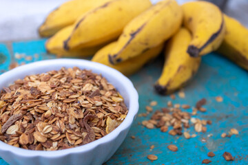 GRANOLA EM TIGELA BRANCA COM BANANAS NO FUNDO.