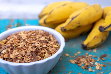 GRANOLA EM TIGELA BRANCA COM BANANAS NO FUNDO.