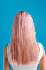 Beautiful sleek natural long pink color dyed hair of young woman standing isolated over blue studio background. Beauty, hair care concept. Back view