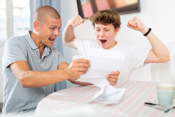 Son and his father sitting at the table and reading letter that contains great news.