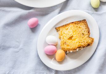 Piece of traditional italian Easter cake Colomba and Easter marzipan eggs in pastel colors, top view with copy space