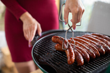 A woman turns the hot sausages lying on the grill.