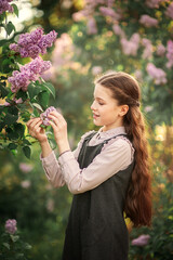 Portrait of cute schoolgirl in school uniform looking at branches of lilac in spring