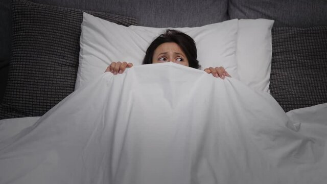 Mature Woman With Dark Hair Lying In Bed And Covering Face With White Blanket. Scared Female By Nightmare Can't Sleep Alone At Home.