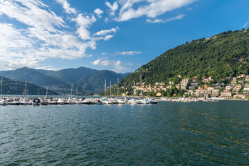 Fototapeta na wymiar View over the beautiful, gorgeous lake Como and the marina seen from the town of Como. It is a beautiful sunny summer day, with blue sky and a few clouds. There are many boats and dinghy in the marina