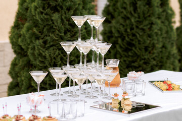 Pyramid of wine glasses. A buffet reception in the open area or on the street for a holiday. A table on which are drinks and snacks. Service or service.
