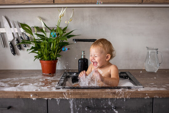 Cute happy baby girl with playing with water and foam in a kitchen sink at home