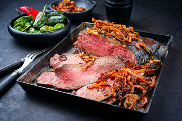Traditional Commonwealth Sunday roast with sliced cold cuts roast beef with fried onion rings and chili served as close-up on an old rustic metal tray