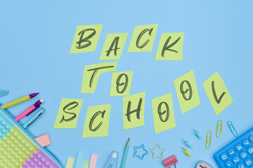 Back to school inscription on cut pieces of yellow paper. Colorful school and office supplies on a blue background. Preschool and school education concept.