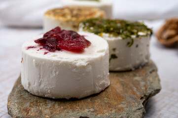 Cheese collection, variety of fresh white soft goat French cheeses with aromatic herbs, berries and green pesto
