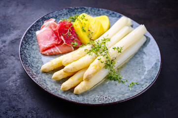 Traditional steamed white asparagus with cured ham and boiled potatoes garnished with butter sauce served as close-up on a Nordic design plate