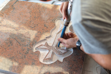 Caucasian man sculptor, bush hammering a granite headstone in a workshop, work concept - obrazy, fototapety, plakaty