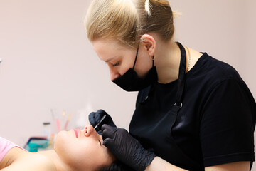 the girl of the master of lamination of cilia sits at the head of the client and performs the...