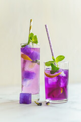 Refreshing summer drink, iced organic blue and violet butterfly pea flower tea with mint and lemons on light vanilla color background. Low shallow focus - 448852387