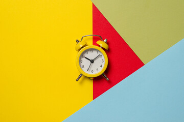 Yellow alarm clock on a yellow, blue, red and green background. Time concept.