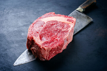 Raw dry aged wagyu rib-eye beef steaks offered as close-up on a large rustic knife with copy space