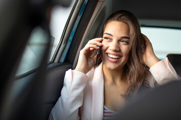 Portrait of a beautiful business woman using a smart phone and smiling while sitting on the back seat of the car. Young woman with smartphone on the back seat of a car