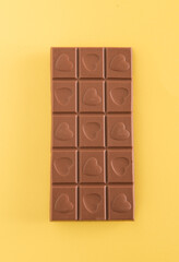Milk chocolate with hearts on it against yellow background. Minimal love concept