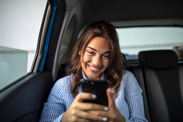 Smiling casual woman sitting in back seat using mobile phone. Cheerful young woman reading messages...