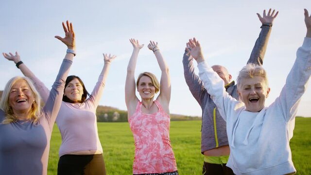 Group of seniors with sport instructor stacking hands after exercise outdoors in nature, active lifestyle.