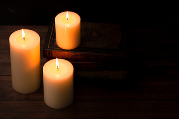 Fototapeta na wymiar Three Pillar Candles Burning in a Dark Room with a Stack of Antique Books