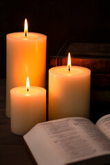 Three Pillar Candles Burning in a Dark Room with a Bible