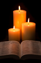 Three Pillar Candles Burning in a Dark Room with a Bible