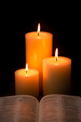 Three Pillar Candles Burning in a Dark Room with a Bible