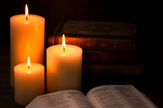 Three Pillar Candles Burning in a Dark Room with a Bible