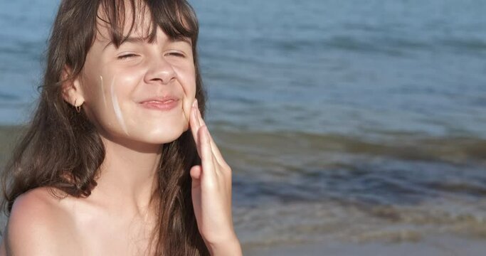 Teen with sunblock. A smiling little girl apply sunblock on her face on the sea shore during summer time.