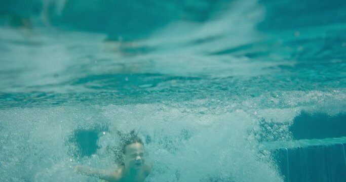 Kids jumping into the pool on summer vacation, family lifestyle at the pool, cinematic slow motion underwater