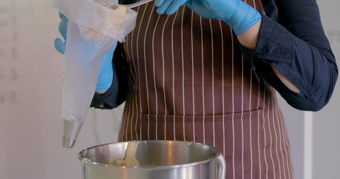 Chef fills confectionery bag with raw pastry dough. The dough for the eclairs fill from pastry bag. Homemade eclairs. Freshly baked crispy oblong eclairs. Homemade sweets. Traditional French eclairs.