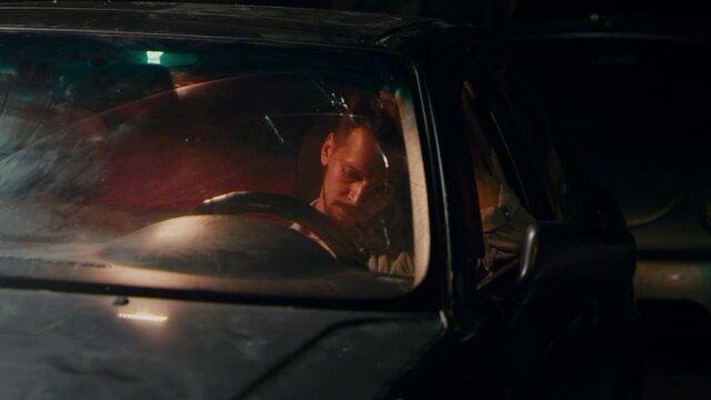 A sad lonely man sits in the car and reads messages on the phone and thinks about something.