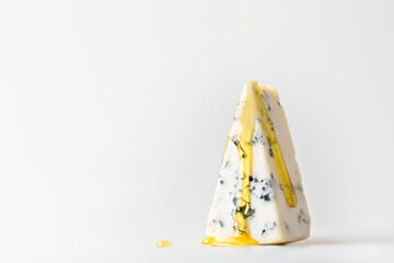 A piece of cheese with blue mold and dripping honey on a light background.