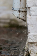 The water falls from the gutter onto the sidewalk