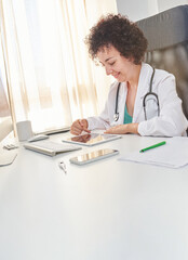 A female doctor uses her digital tablet sitting at the desk in her medical office